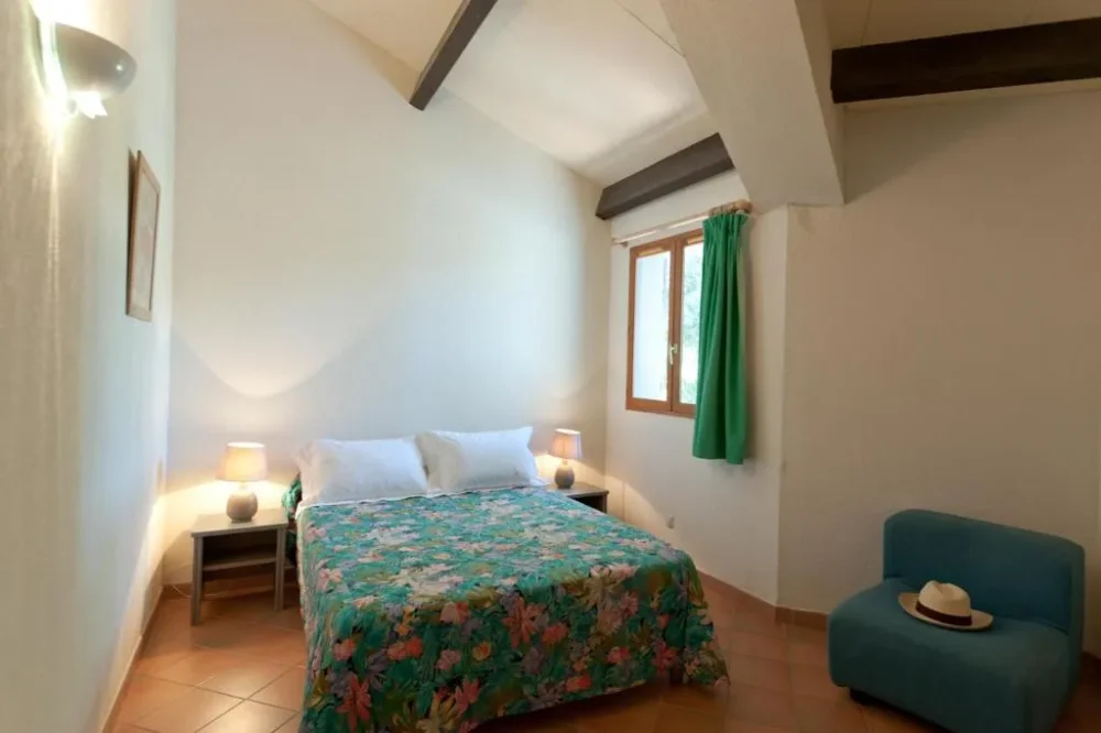 Chambre avec lit double, fauteuil et fenêtre.