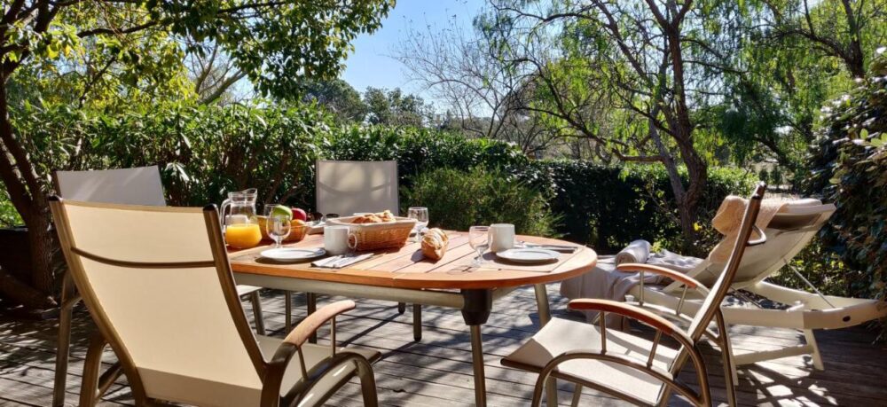 Petit déjeuner en terrasse ensoleillée avec nature environnante.