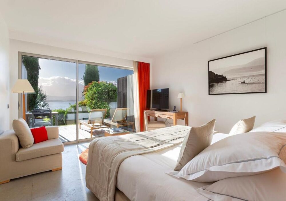 Chambre lumineuse avec vue sur terrasse et lac.