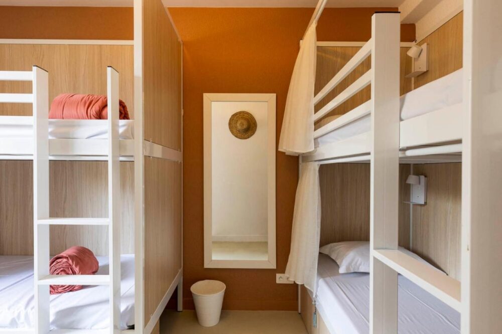 Chambre dortoir avec lits superposés et miroir mural.