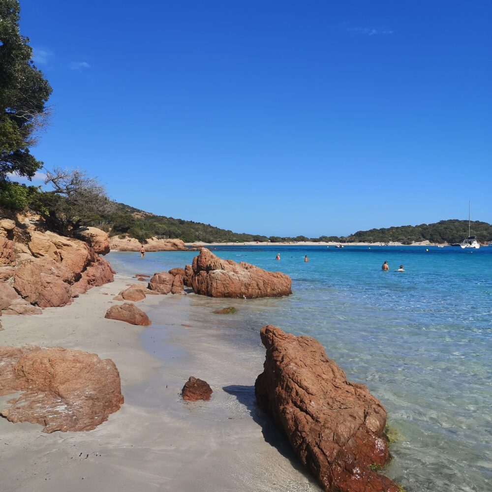 Plage avec rochers et eau turquoise, ciel bleu.