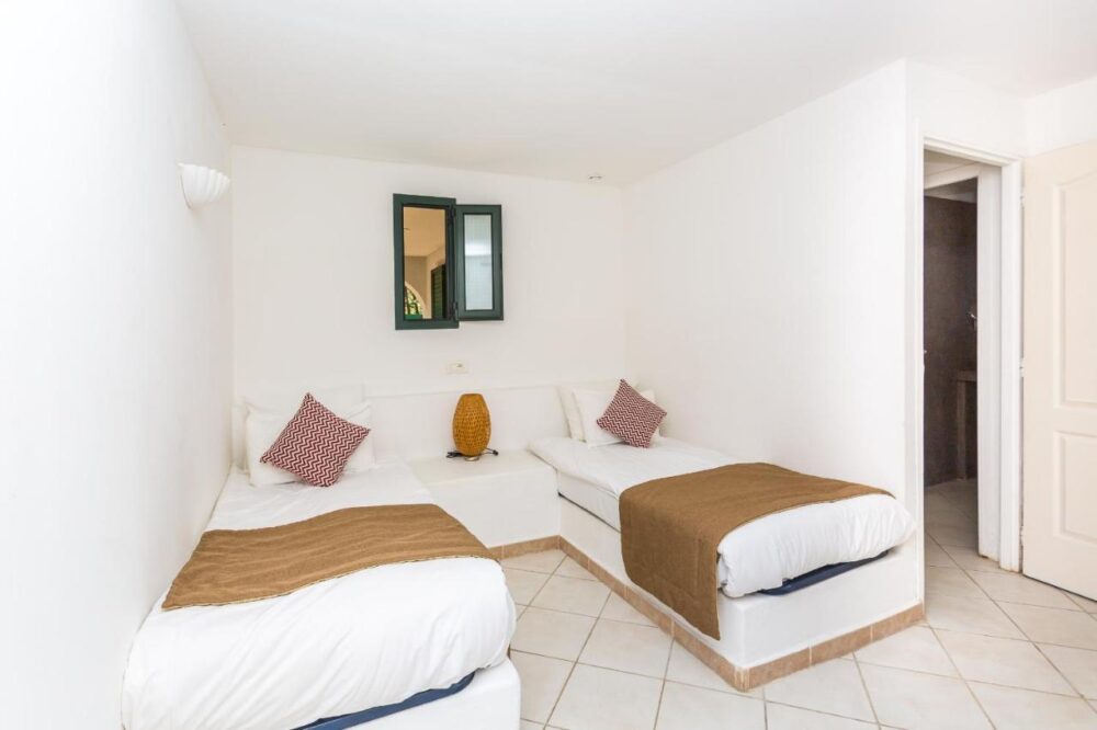 Chambre blanche avec deux lits simples et fenêtres.