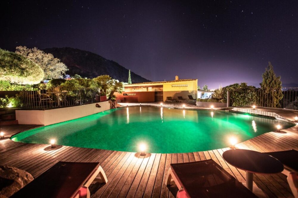 Piscine éclairée la nuit avec terrasse en bois.