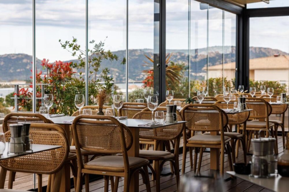 Restaurant vitré avec vue panoramique et tables dressées.