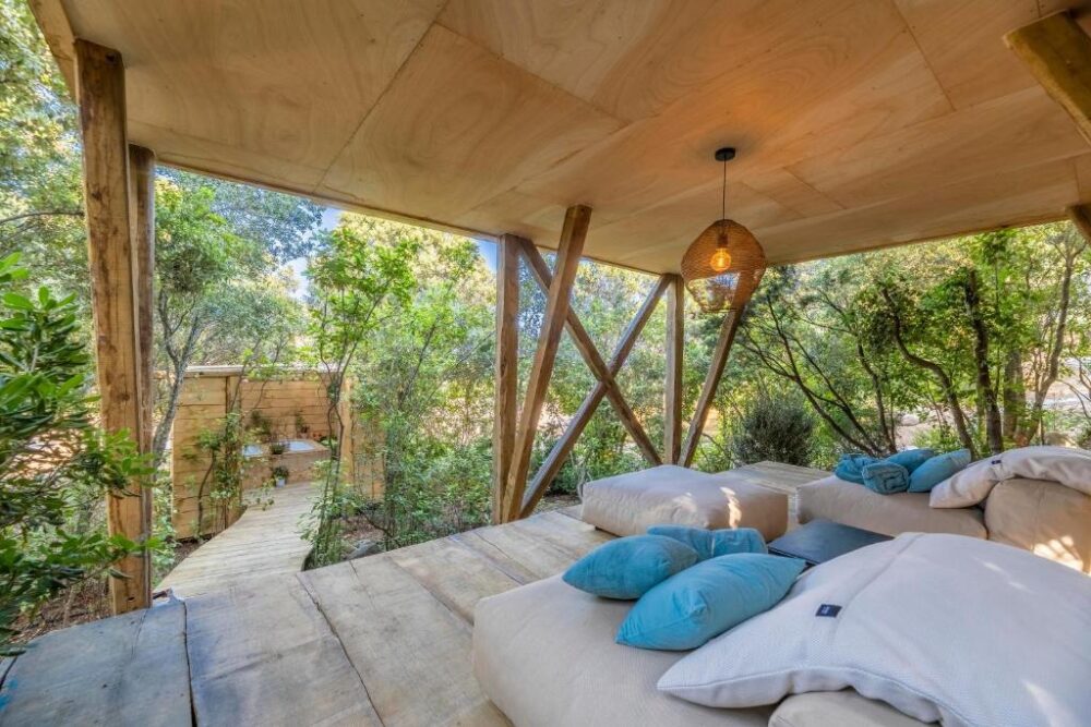 Terrasse en bois avec coussins et nature environnante.