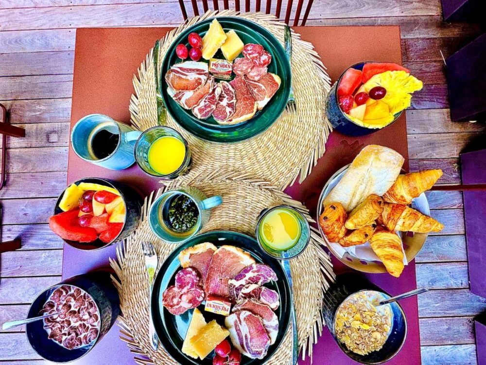 Petit-déjeuner varié avec fruits, charcuterie, et croissants.