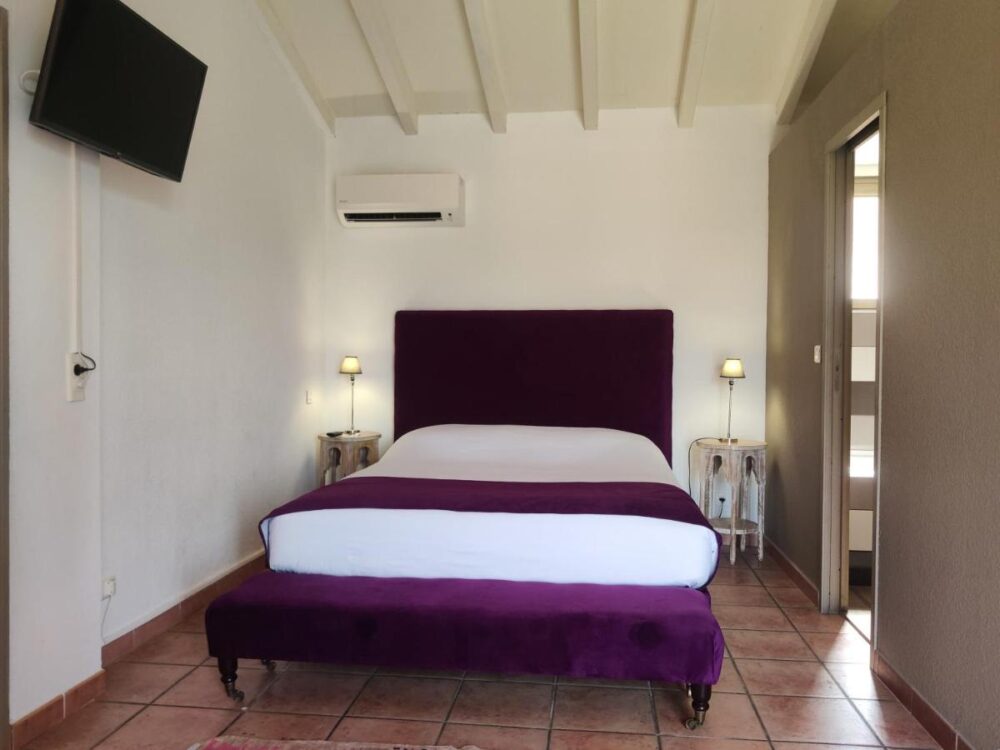 Chambre double avec lit violet et télé murale.