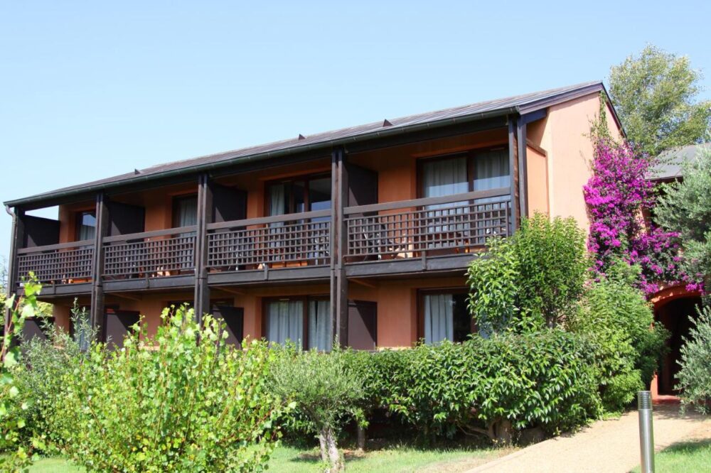 Bâtiment résidentiel avec balcons et jardin verdoyant.