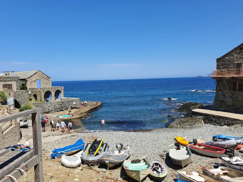 Plage rocheuse avec maisons en pierres et barques.