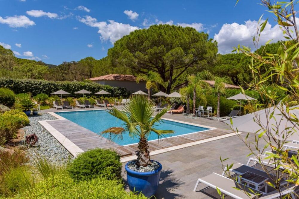 Piscine extérieure entourée de chaises longues et arbres.