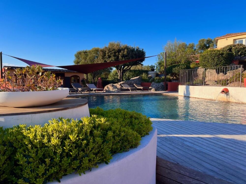 Piscine extérieure entourée de verdure et chaises longues.