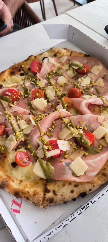 Pizza garnie de mortadelle, pistaches et tomates cerises.