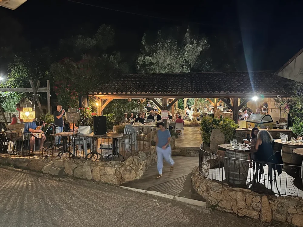 Restaurant extérieur avec musiciens et convives le soir.