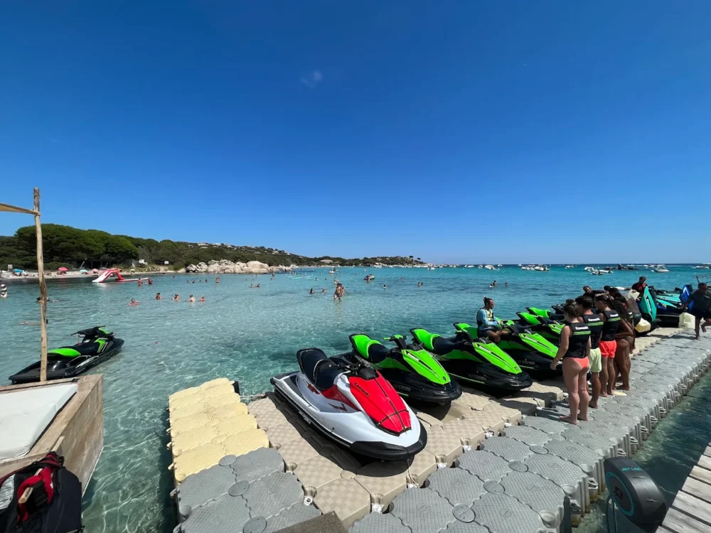 Jet-skis alignés sur un ponton, plage en arrière-plan.